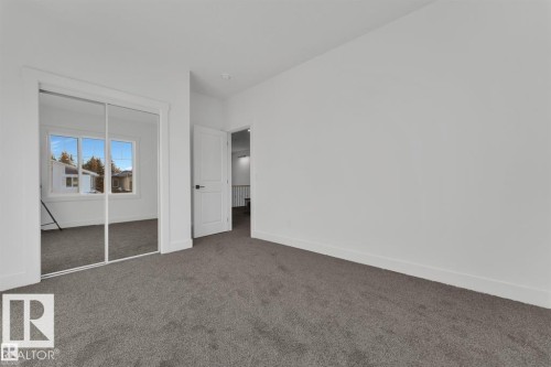 Spacious room featuring neutral carpeting, white trim, and a white interior door with dark hardware - 1129 Starling Drive, Edmonton, AB 