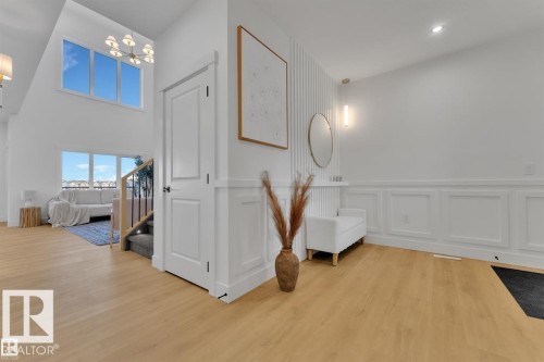 Spacious entry foyer featuring light wood-finish flooring, white wainscoting, and a contemporary pendant light fixture - 1129 Starling Drive, Edmonton, AB 