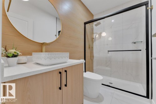 Modern bathroom featuring a glass-enclosed shower with black trim, a contemporary vessel sink, a light wood-finish vanity with a white countertop, and an oval mirror with a gold frame - 1129 Starling Drive, Edmonton, AB 