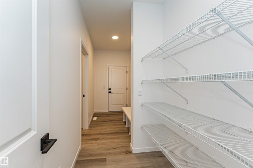 This entry area features wood-effect flooring and a white door with black hardware, leading to a space with wire shelving - 2355 Egret Way, Edmonton, AB - Indoor Photo Showing Other Room