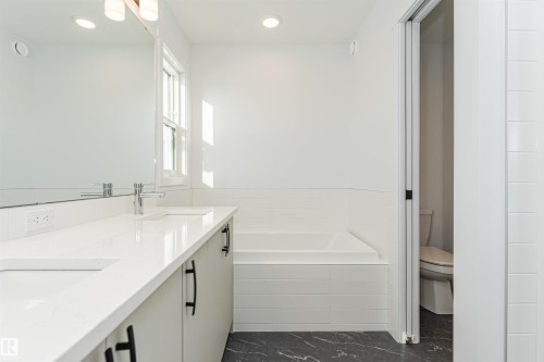 The bathroom features a double vanity with white countertops, a built-in bathtub, and dark patterned flooring - 2355 Egret Way, Edmonton, AB - Indoor Photo Showing Bathroom