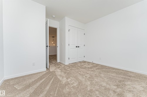 This room features plush carpet flooring, bright white walls, and white bi-fold closet doors with black hardware - 2355 Egret Way, Edmonton, AB - Indoor Photo Showing Other Room