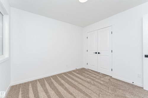 This room features bright white walls, a window providing natural light, and patterned carpeting - 2355 Egret Way, Edmonton, AB - Indoor Photo Showing Other Room