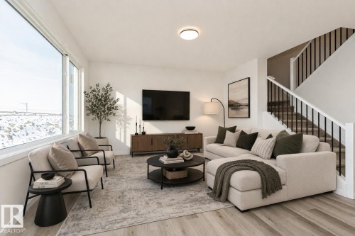 The property features an open living space with light-colored flooring, a large window providing natural light, and a staircase with dark balusters - 2355 Egret Way, Edmonton, AB - Indoor Photo Showing Living Room