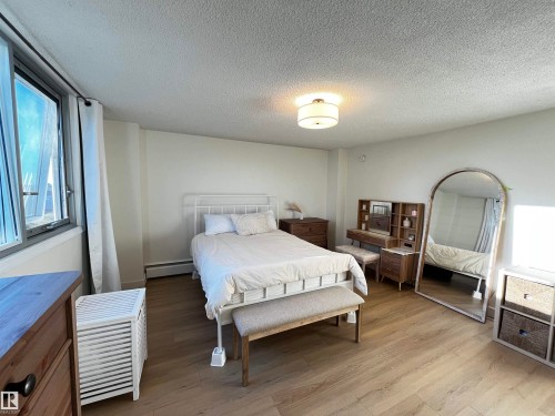 Bedroom featuring wood-finish flooring, a contemporary ceiling light fixture, and a large window with white curtains - 807 10011 116 Street, Edmonton, AB - Indoor Photo Showing Bedroom