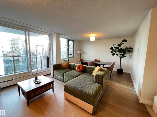 Spacious living area featuring large windows, wood-finish flooring, a ceiling-mounted light fixture, and a dedicated dining space - 807 10011 116 Street, Edmonton, AB - Indoor Photo Showing Living Room