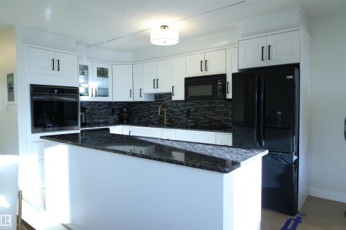Modern kitchen featuring white cabinetry with dark hardware, a dark stone countertop, a dark tile backsplash, a built-in oven, and a black refrigerator - 807 10011 116 Street, Edmonton, AB - Indoor Photo Showing Kitchen With Upgraded Kitchen