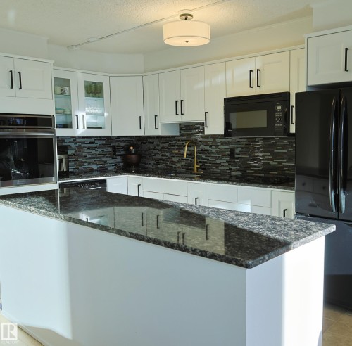 Kitchen featuring white cabinetry with black hardware, dark speckled countertops, a multi-tone tile backsplash, and a gold-tone faucet - 807 10011 116 Street, Edmonton, AB - Indoor Photo Showing Kitchen With Upgraded Kitchen
