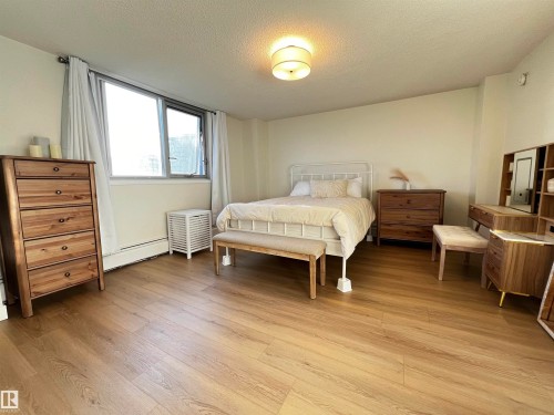Spacious room featuring wood-finish flooring, a large window with white curtains, and a ceiling-mounted drum light fixture - 807 10011 116 Street, Edmonton, AB - Indoor Photo Showing Bedroom