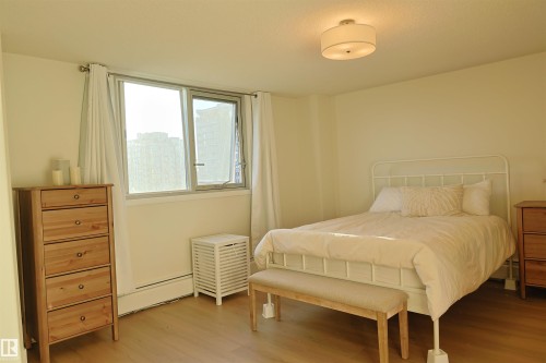 Bright interior space featuring a window with white curtains, wood-finish flooring, and a flush-mount ceiling light fixture - 807 10011 116 Street, Edmonton, AB - Indoor Photo Showing Bedroom