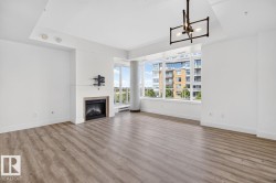 Living area featuring wood-finish flooring, a contemporary fireplace with a light-toned surround, expansive windows, and a modern chandelier - 