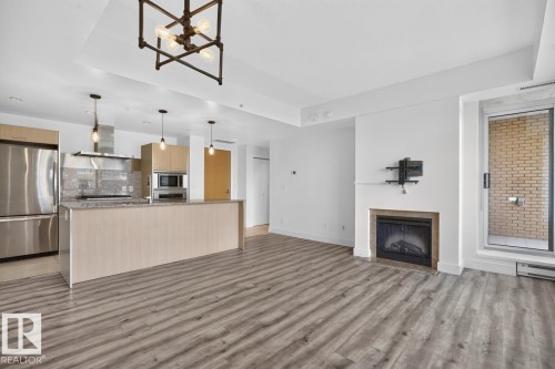 Open-concept living space featuring wood-finish flooring, a contemporary kitchen island, stainless steel appliances, and a built-in fireplace - #407 2504 109 St Nw, Edmonton, AB - Indoor With Fireplace
