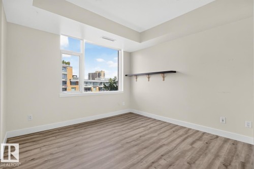 Room featuring large windows, wood-finish flooring, light-colored walls, white baseboards, and a wall-mounted dark-toned shelf - #407 2504 109 St Nw, Edmonton, AB - Indoor Photo Showing Other Room