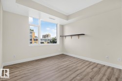 Room featuring large windows, wood-finish flooring, light-colored walls, white baseboards, and a wall-mounted dark-toned shelf - 