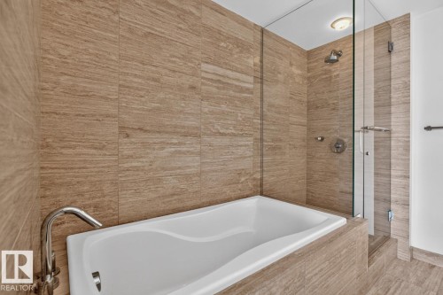 Modern bathroom featuring a built-in soaking tub with a polished chrome faucet, full-height tile surround, and a glass-enclosed shower with a rainfall showerhead - #407 2504 109 St Nw, Edmonton, AB - Indoor Photo Showing Bathroom