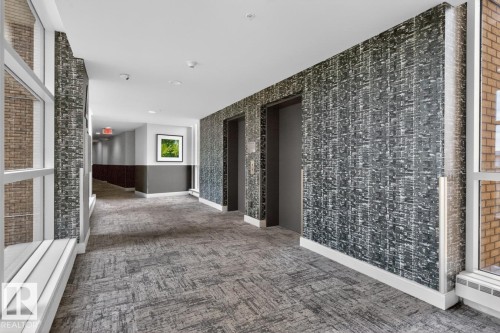 Hallway featuring patterned wall covering, two elevator doors, large windows, recessed lighting, and patterned carpet flooring - #407 2504 109 St Nw, Edmonton, AB - Indoor Photo Showing Other Room