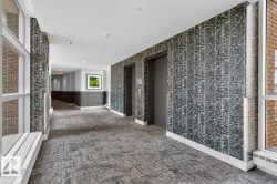 Hallway featuring patterned wall covering, two elevator doors, large windows, recessed lighting, and patterned carpet flooring - 