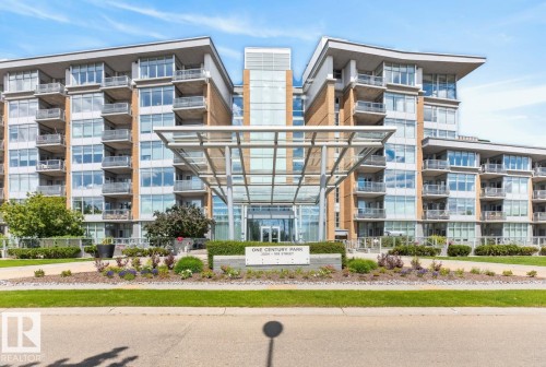 Modern condominium building featuring a striking glass-enclosed main entrance, multiple levels of private balconies, a contemporary glass and metal porte-cochère, expansive window-lined facades, and manicured landscaping with decorative plantings - #407 2504 109 St Nw, Edmonton, AB - Outdoor With Balcony With Facade