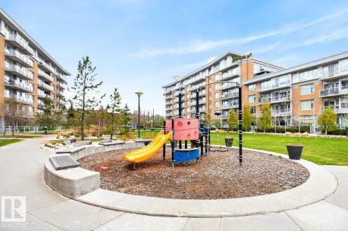 Central playground featuring a yellow slide and climbing structure, surrounded by a concrete border and wood chip ground cover - #407 2504 109 St Nw, Edmonton, AB - Outdoor With Balcony