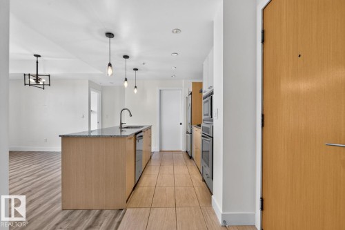 Contemporary kitchen with a central island featuring a sink and integrated dishwasher, granite-finish countertop, and pendant lighting - #407 2504 109 St Nw, Edmonton, AB - Indoor Photo Showing Kitchen