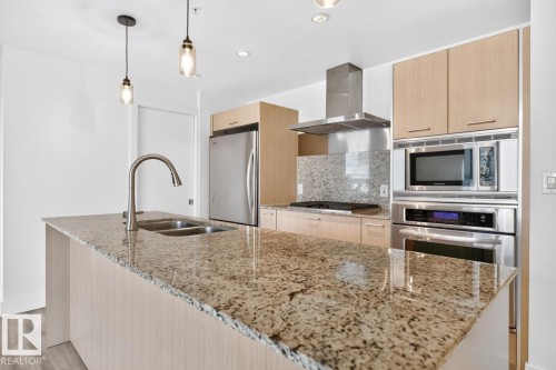 Spacious kitchen island featuring a dual-basin stainless steel sink with a gooseneck faucet, granite countertops, light wood-finish cabinetry, stainless steel appliances, and pendant lighting - #407 2504 109 St Nw, Edmonton, AB - Indoor Photo Showing Kitchen With Double Sink With Upgraded Kitchen