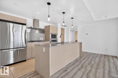 Open-concept kitchen featuring an island with an undermount sink, stainless steel appliances, light wood-finish cabinetry, and recessed lighting - #407 2504 109 St Nw, Edmonton, AB - Indoor Photo Showing Kitchen With Upgraded Kitchen