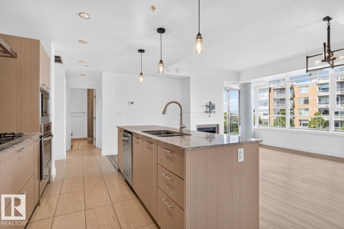 Open-concept kitchen with light wood-finish cabinetry, built-in stainless steel appliances, and a central island featuring a double-basin sink and granite-style countertop - #407 2504 109 St Nw, Edmonton, AB - Indoor Photo Showing Kitchen With Double Sink With Upgraded Kitchen