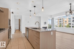Open-concept kitchen with light wood-finish cabinetry, built-in stainless steel appliances, and a central island featuring a double-basin sink and granite-style countertop - 