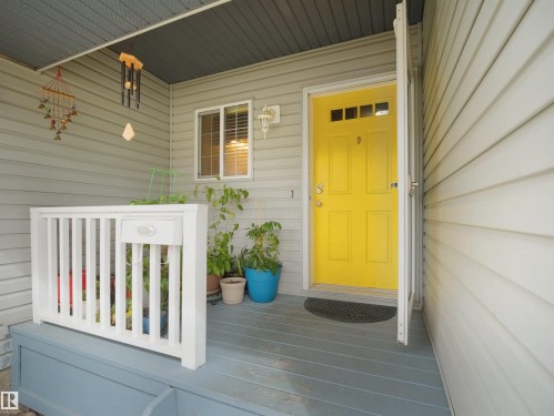 Welcoming front porch featuring a vibrant yellow entry door with upper lites, durable siding, and a painted wood deck - 16121 131A Street, Edmonton, AB - Outdoor With Exterior