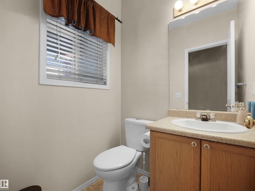 Powder room featuring a single-pane window with horizontal blinds, a wood-finish vanity with a built-in sink, a speckled countertop, and an overhead light fixture - 16121 131A Street, Edmonton, AB - Indoor Photo Showing Bathroom