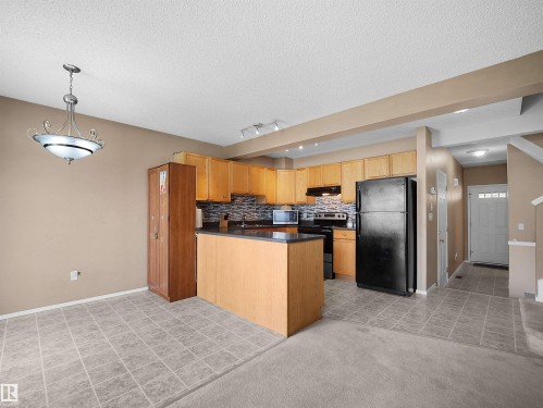 Open-concept kitchen and dining area featuring light wood cabinetry, dark countertops, a dark tile backsplash, and a central island - 16121 131A Street, Edmonton, AB - Indoor Photo Showing Kitchen