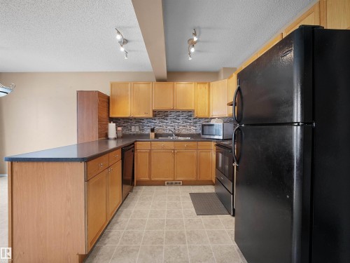 Kitchen featuring natural wood cabinetry, a dark countertop, and a mosaic tile backsplash - 16121 131A Street, Edmonton, AB - Indoor Photo Showing Kitchen