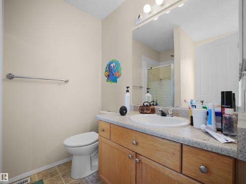 Bathroom featuring a wood-finish vanity with an integrated sink and light-toned countertop, a wall-mounted mirror with overhead lighting, and a walk-in shower with a glass enclosure - 16121 131A Street, Edmonton, AB - Indoor Photo Showing Bathroom