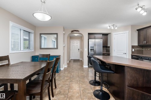 Open-concept interior featuring tile flooring, a kitchen island with seating, dark wood-finish cabinetry, stainless steel appliances, and a tiled backsplash - 2007 74 Street, Edmonton, AB - Indoor Photo Showing Dining Room