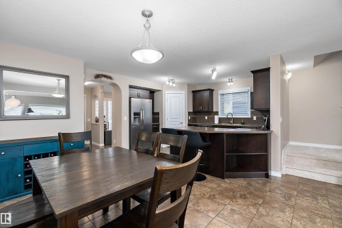 Kitchen and dining area featuring dark wood cabinetry, stainless steel appliances, a kitchen island with built-in shelving, tile flooring, and track lighting - 2007 74 Street, Edmonton, AB - Indoor Photo Showing Dining Room