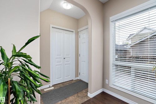 Entryway featuring an arched doorway, white bi-fold doors, a large window with blinds, and mixed flooring transitions - 2007 74 Street, Edmonton, AB - Indoor