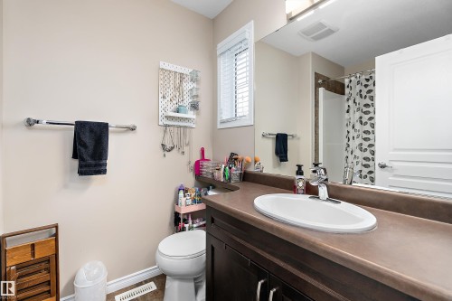 En suite featuring a dark wood-finish vanity with an integrated sink, a large wall-mounted mirror, and a window with horizontal blinds - 2007 74 Street, Edmonton, AB - Indoor Photo Showing Bathroom