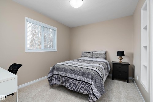 Neutral-toned room featuring a window with white blinds, light-colored carpet, recessed shelving, and a flush-mount ceiling light fixture - 2007 74 Street, Edmonton, AB - Indoor Photo Showing Bedroom