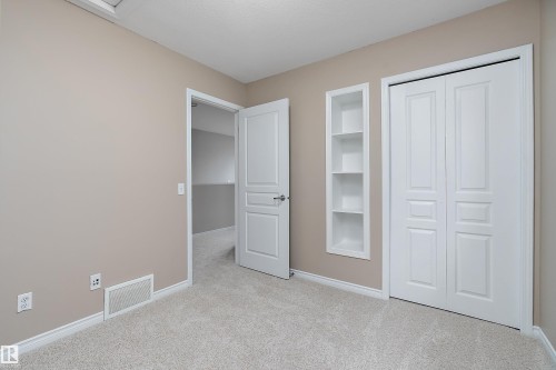 Carpeted room featuring a neutral wall color, white trim, a built-in shelving unit, and bifold closet doors - 2007 74 Street, Edmonton, AB - Indoor