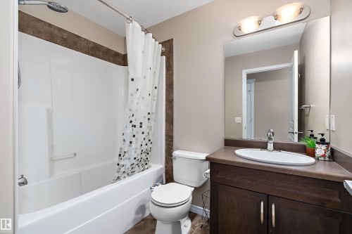 Full bathroom featuring a white tub and shower combination with a textured accent wall, a dark wood-finish vanity with an oval sink, a wall-mounted mirror, and a two-bulb vanity light fixture - 2007 74 Street, Edmonton, AB - Indoor Photo Showing Bathroom