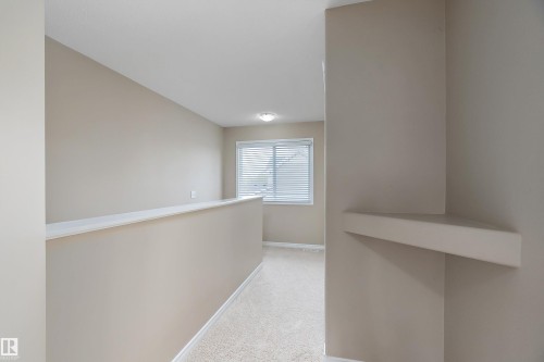 Carpeted hallway featuring light neutral wall tones, a window with blinds, and a built-in corner shelf - 2007 74 Street, Edmonton, AB - Indoor Photo Showing Other Room