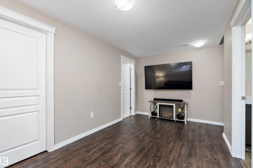 Interior space featuring wood-finish flooring, a wall-mounted display, and a modern console with an electric fireplace - 2007 74 Street, Edmonton, AB - Indoor Photo Showing Living Room With Fireplace