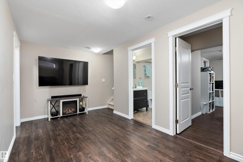 Spacious room featuring wood-finish flooring, a wall-mounted television, and an electric fireplace set into a media console - 2007 74 Street, Edmonton, AB - Indoor With Fireplace
