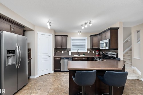 Kitchen featuring dark wood cabinetry, stainless steel appliances, a breakfast bar, patterned tile flooring, and a tile backsplash - 2007 74 Street, Edmonton, AB - Indoor Photo Showing Kitchen With Stainless Steel Kitchen