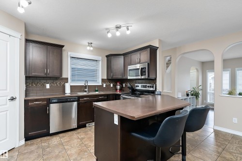 Kitchen featuring a central island, dark wood cabinetry, stainless steel appliances, and tiled flooring - 2007 74 Street, Edmonton, AB - Indoor Photo Showing Kitchen With Stainless Steel Kitchen