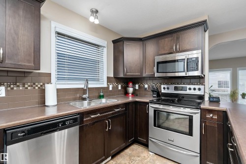 Kitchen featuring rich wood-finish cabinetry, stainless steel appliances, and a mosaic tile backsplash - 2007 74 Street, Edmonton, AB - Indoor Photo Showing Kitchen With Stainless Steel Kitchen With Double Sink