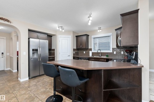 Kitchen featuring a multi-toned tile floor, dark wood-finish cabinetry, a stainless steel side-by-side refrigerator, and an island with built-in shelving - 2007 74 Street, Edmonton, AB - Indoor Photo Showing Kitchen With Stainless Steel Kitchen