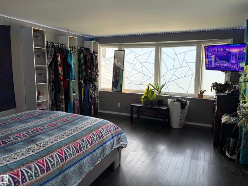 Spacious room featuring dark wood-finish flooring, a wide window with geometric privacy film, and built-in vertical shelving units - 4108 49 Avenue, Bonnyville Town, AB - Indoor Photo Showing Bedroom