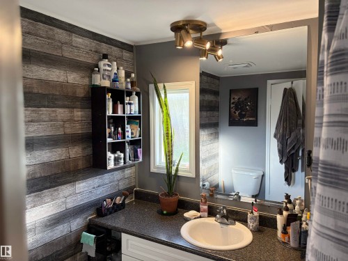 Bathroom featuring a vanity with an integrated sink, a dark speckled countertop, and a large wall-mounted mirror - 4108 49 Avenue, Bonnyville Town, AB - Indoor