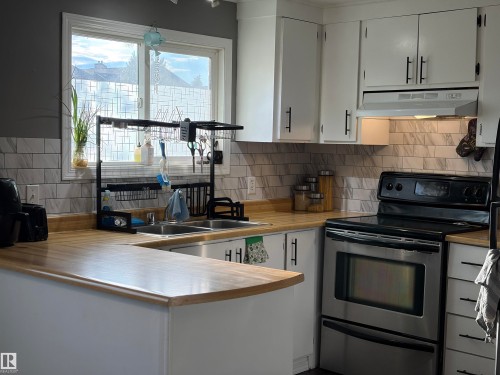 Kitchen featuring light wood-finish countertops, subway tile backsplash, white cabinetry with black hardware, and a stainless steel electric range - 4108 49 Avenue, Bonnyville Town, AB - Indoor Photo Showing Kitchen With Double Sink